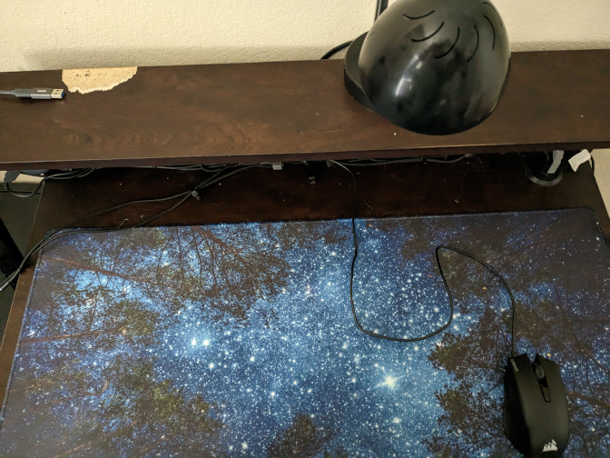 An overview of a blank desk with a deskmat, lamp, and mouse